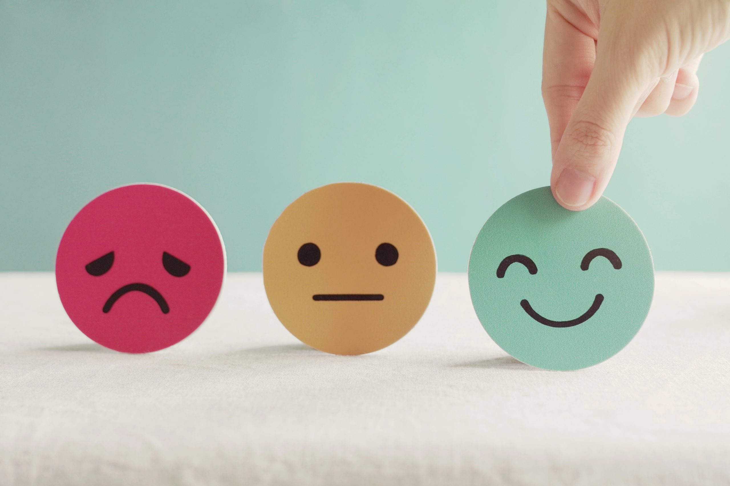 Person pointing towards three emojis, one frowning, one with a blank expression and one smiling